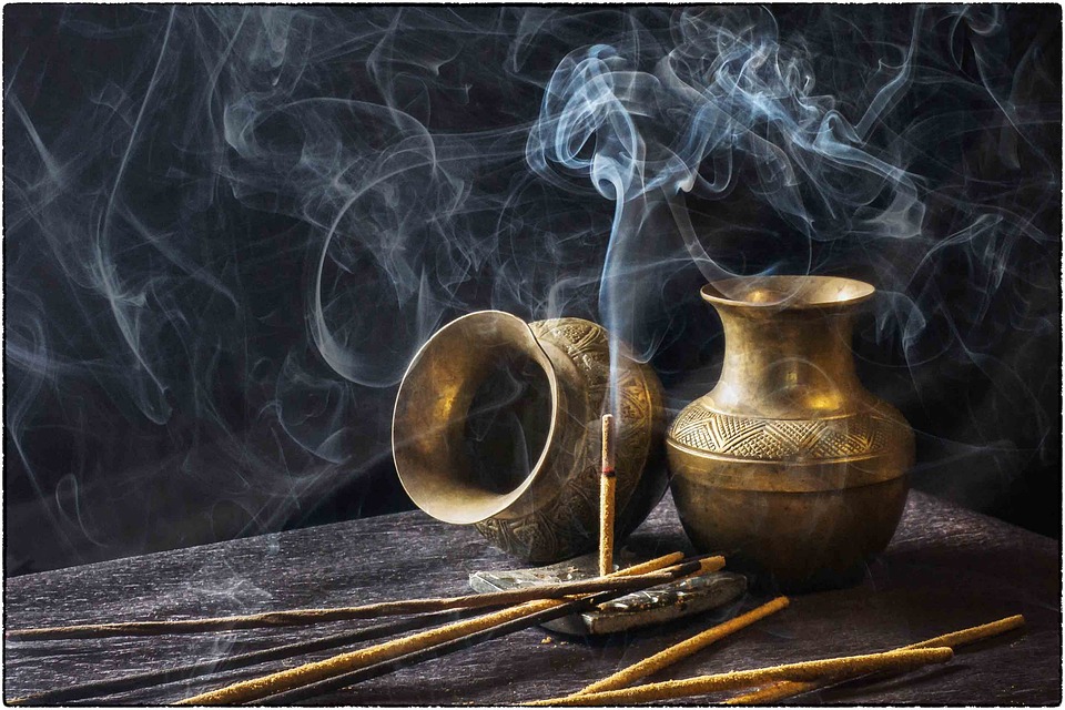 Bâtons d'encens et fumée avec vases en bronze sur fond noir.